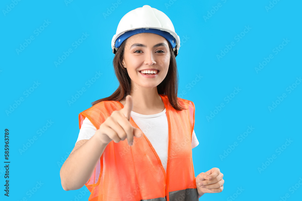 Female worker in vest pointing at viewer on blue background