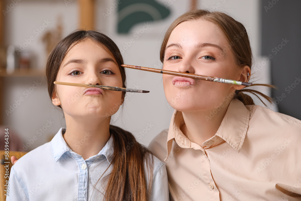 Funny little girl and her drawing teacher with paint brushes in workshop, closeup