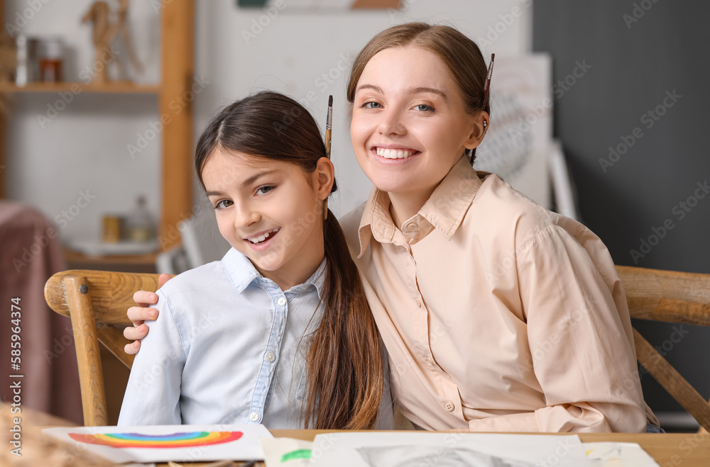 Little girl and her drawing teacher with paint brushes in workshop