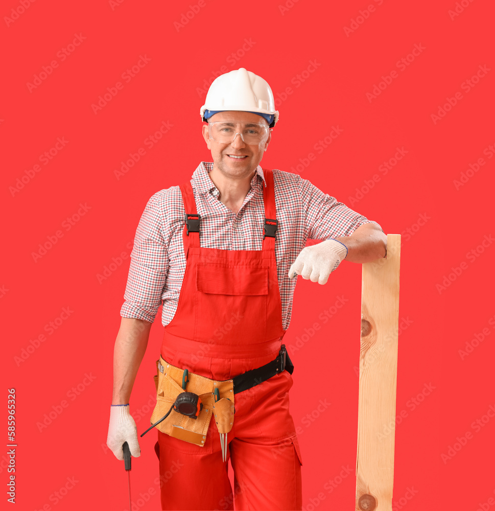 Mature carpenter with hacksaw and wooden plank on red background