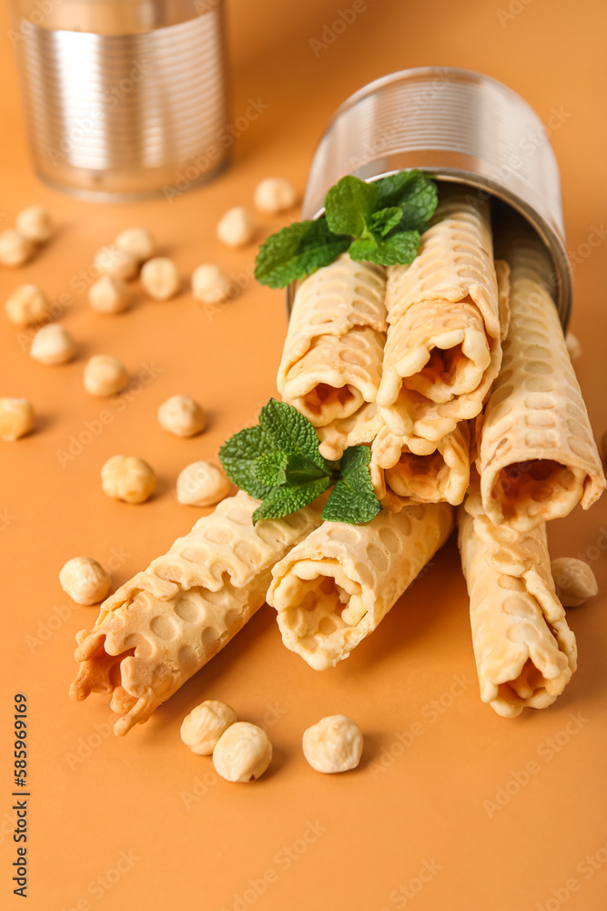 Overturned tin can with delicious wafer rolls on orange background