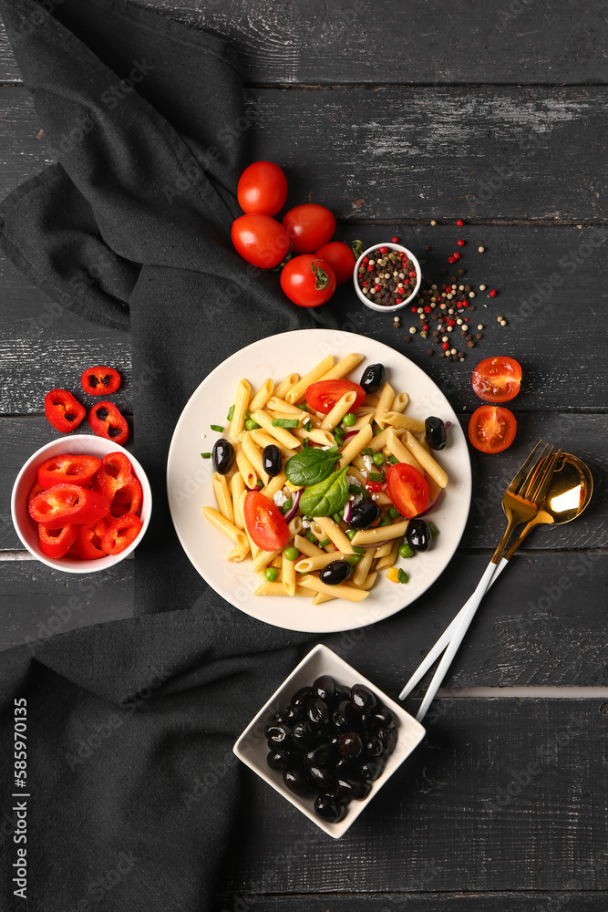 Plate with tasty pasta salad and ingredients on dark wooden background