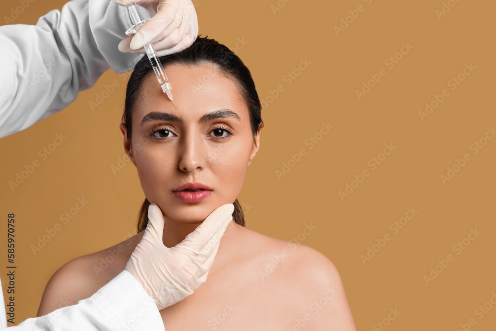 Young woman receiving filler injection in face against beige background