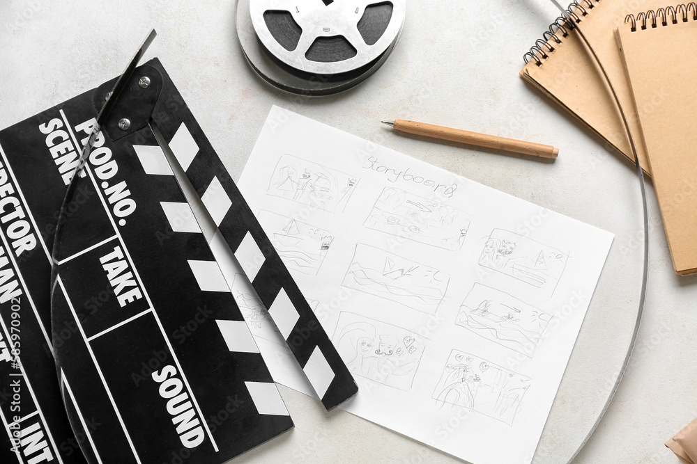 Movie clapper with storyboard, notebooks and film reel on light background