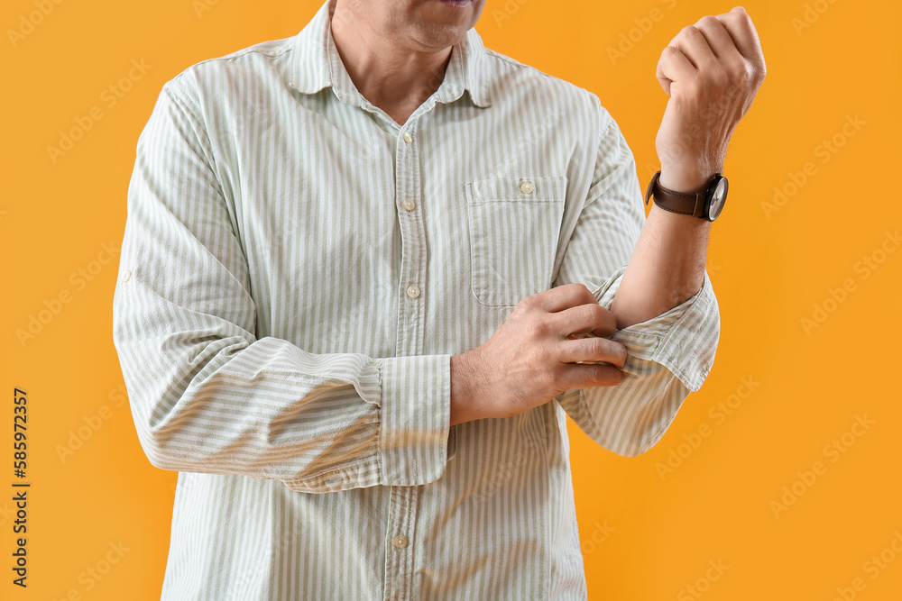 Mature man rolling up his sleeve on yellow background, closeup