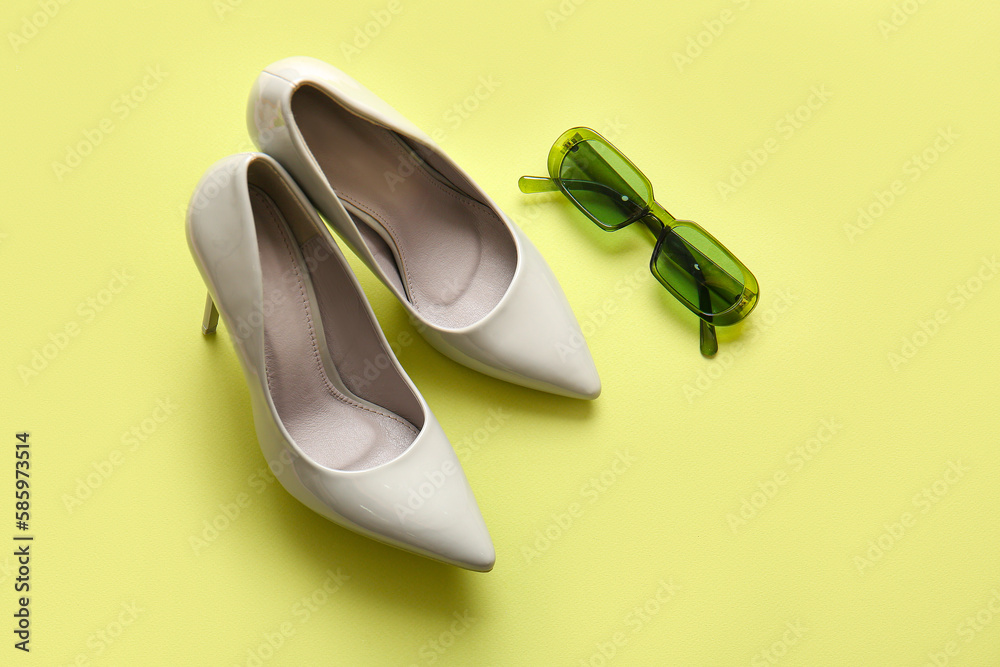 Stylish high heeled shoes and sunglasses on green background