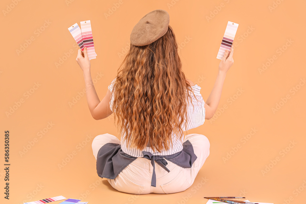 Female artist with paint color palettes sitting on beige background, back view