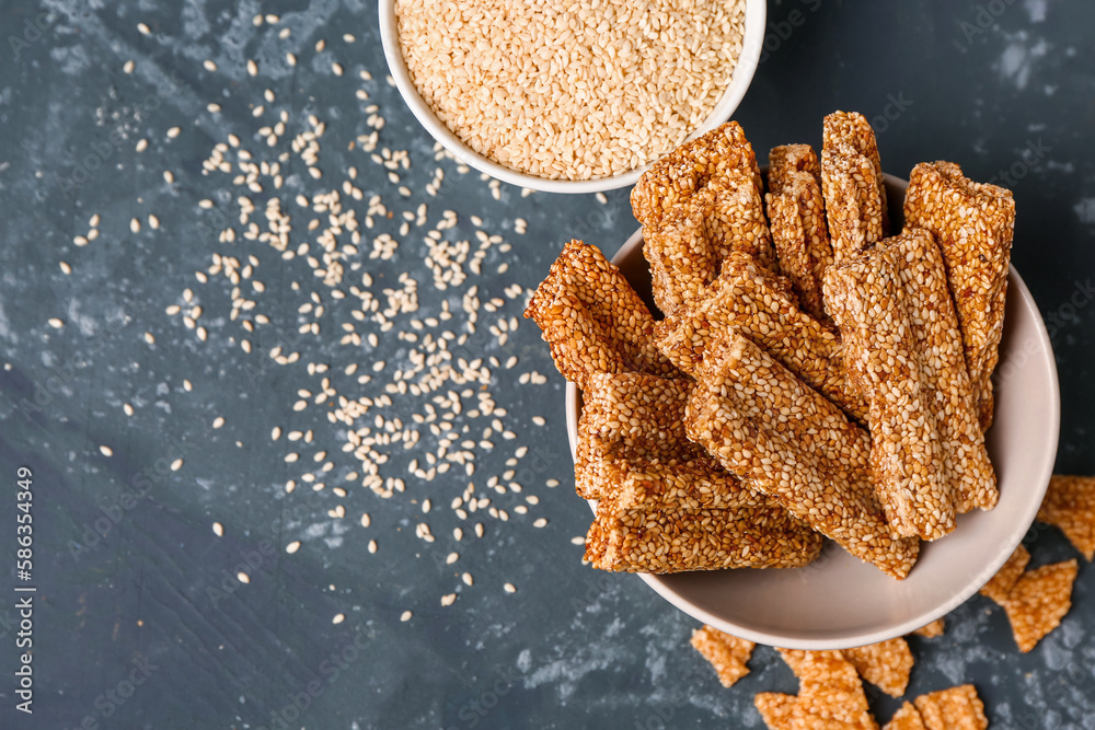 Bowls of tasty kozinaki and sesame seeds on blue background