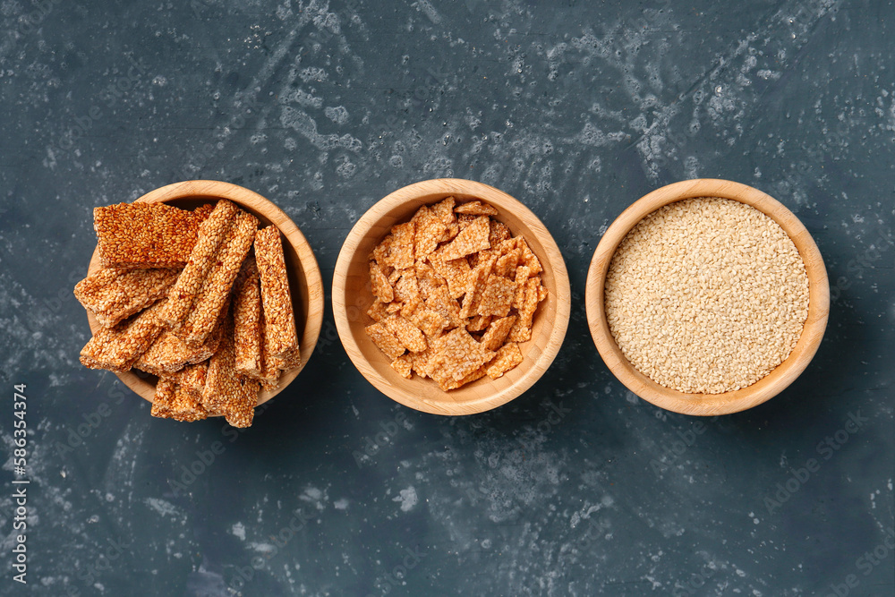 Bowls of tasty kozinaki and sesame seeds on blue background