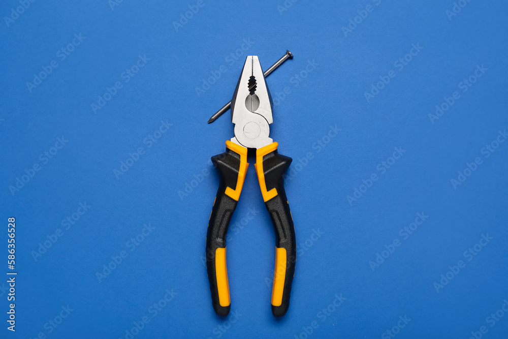 Pliers with nail on blue background