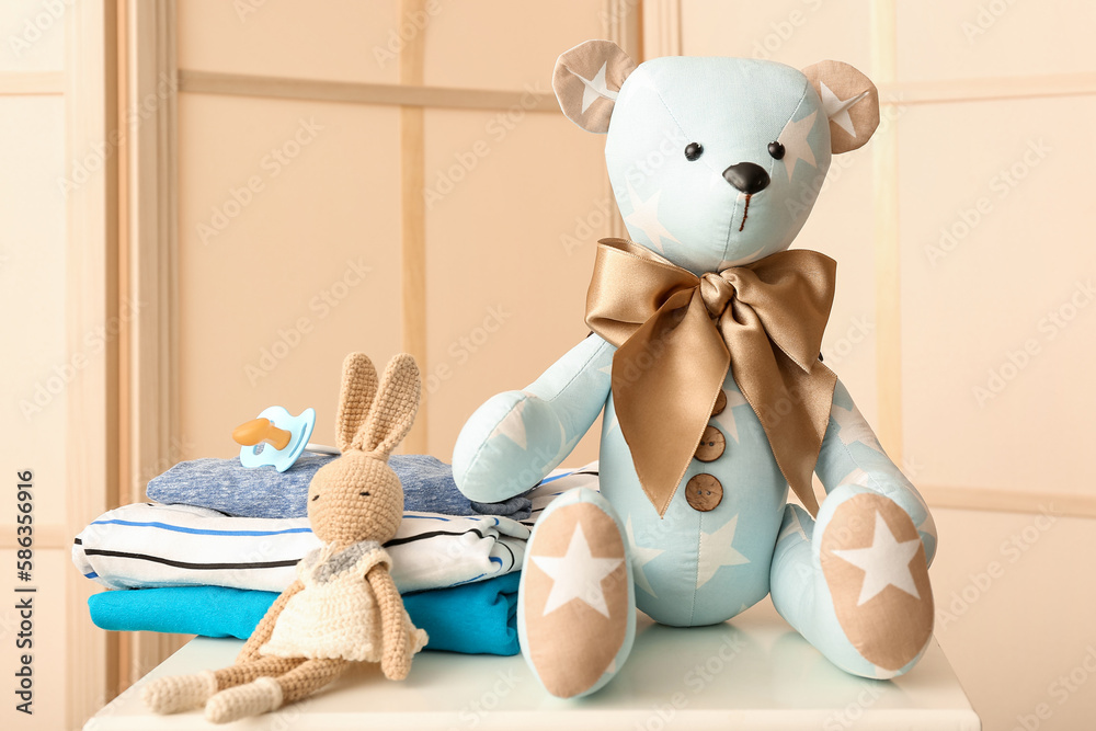 Toy bear with bunny and baby clothes on shelf in room