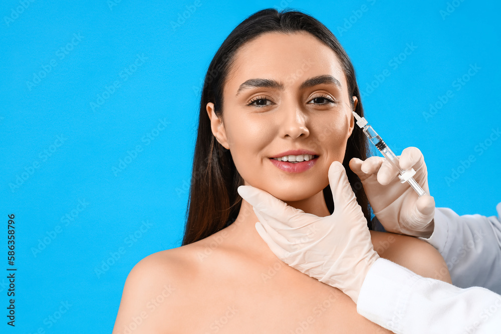 Young woman receiving filler injection in face against blue background