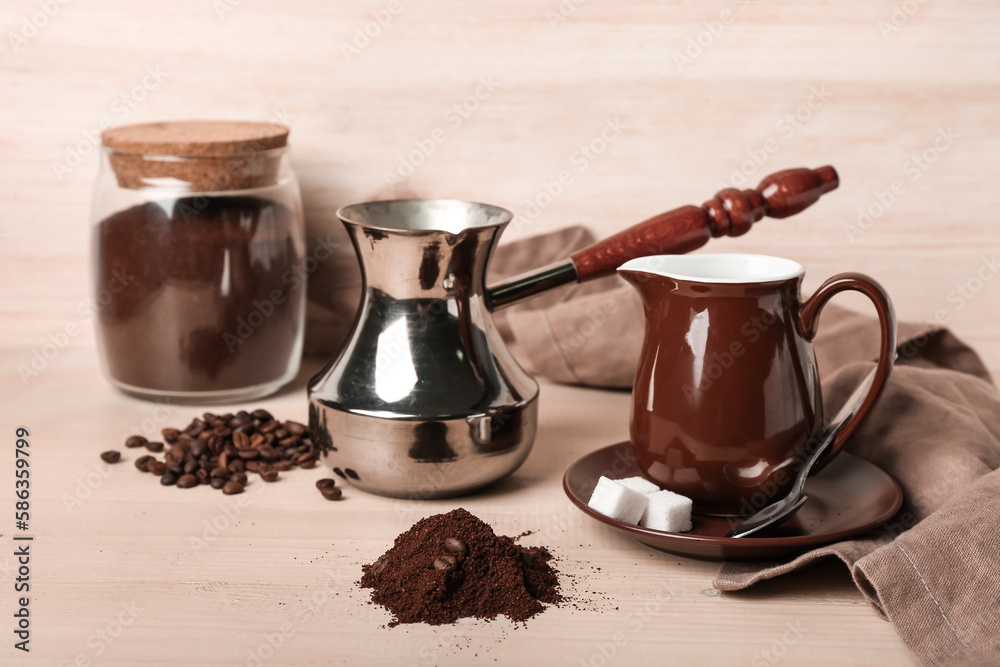 Cezve with coffee powder, beans, jar and milk jug on light wooden table