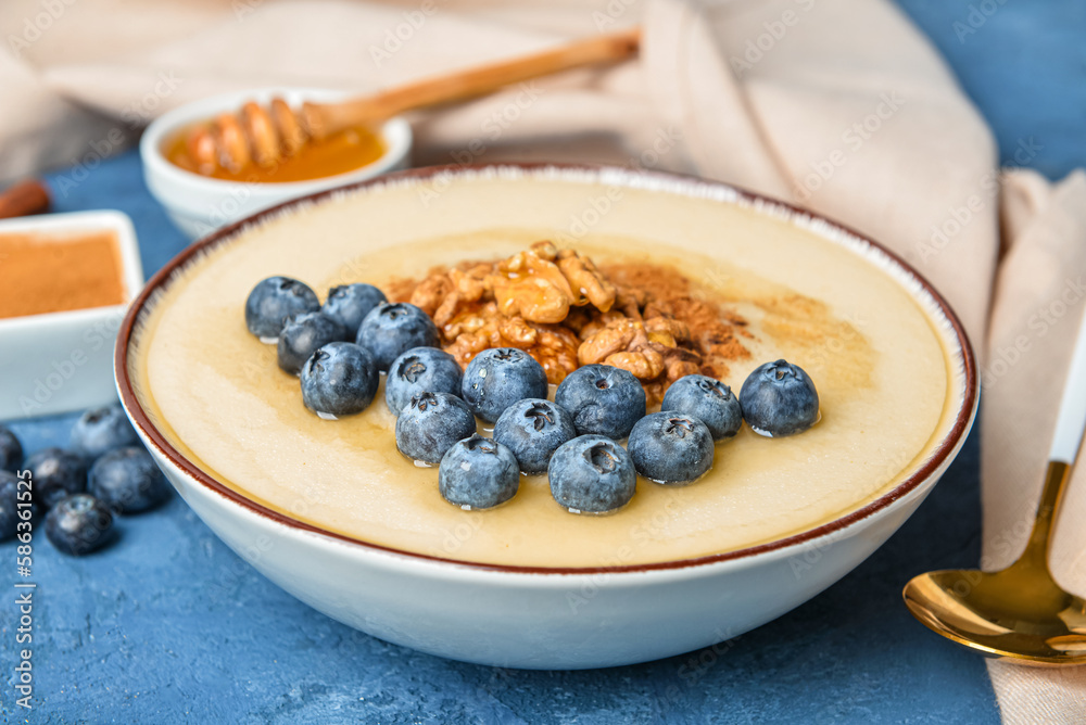 Bowl of tasty semolina porridge with blueberry, cinnamon, nuts and honey on color table