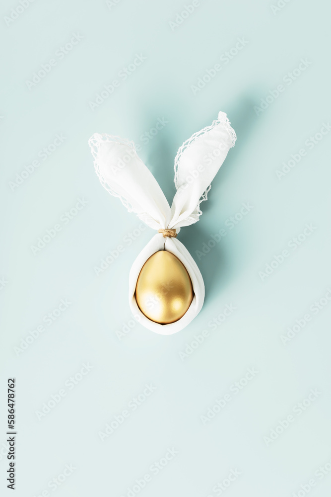 Stylish Easter flat lay with golden egg in easter bunny napkin over blue background. Minimalist mode