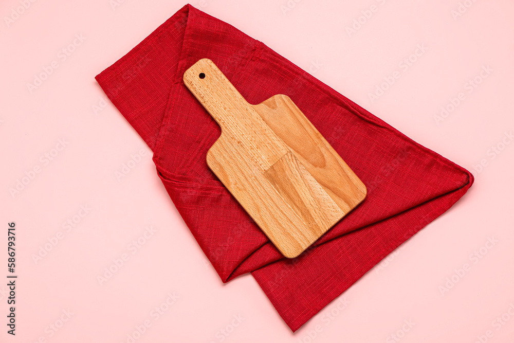 Wooden cutting board and napkin on pink background