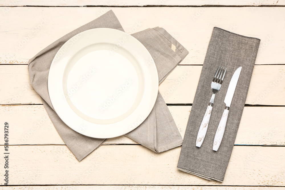 Plate, cutlery and napkins on light wooden background