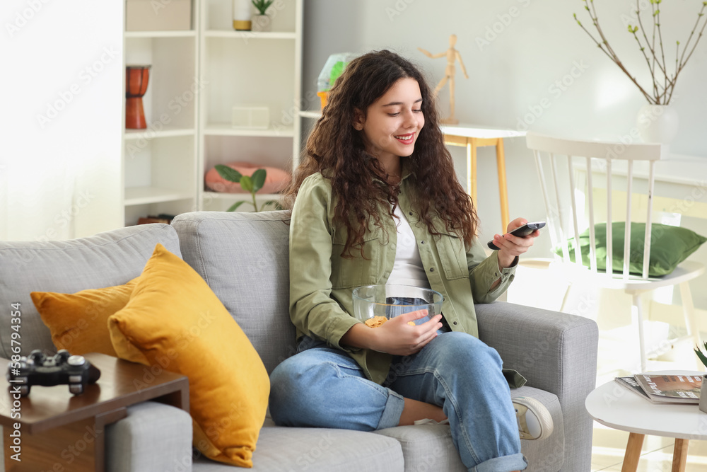 Teenage girl with bowl of chips watching TV at home