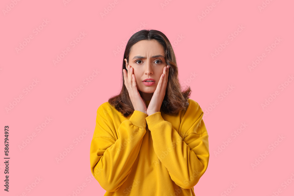 Upset young woman in yellow sweatshirt on pink background