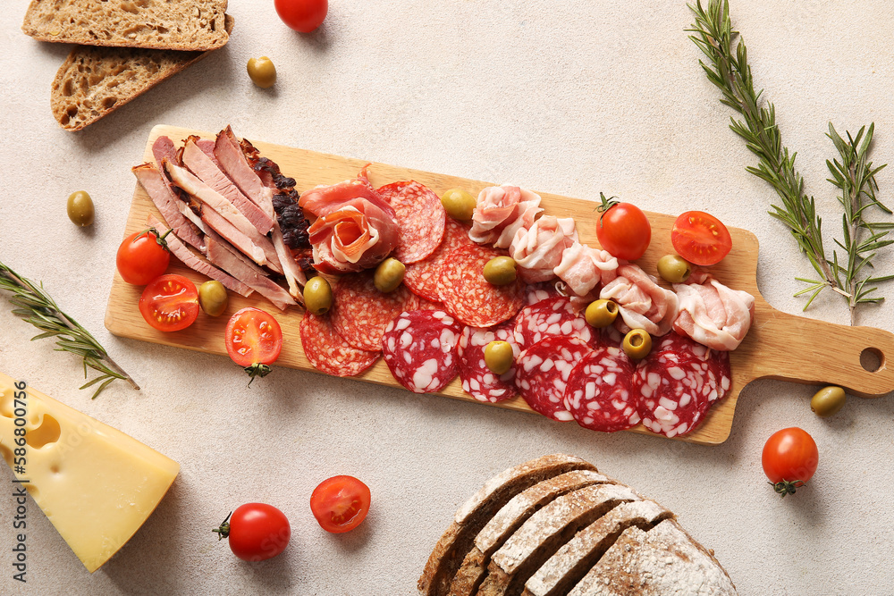 Wooden board with assortment of tasty deli meats and bread on light background