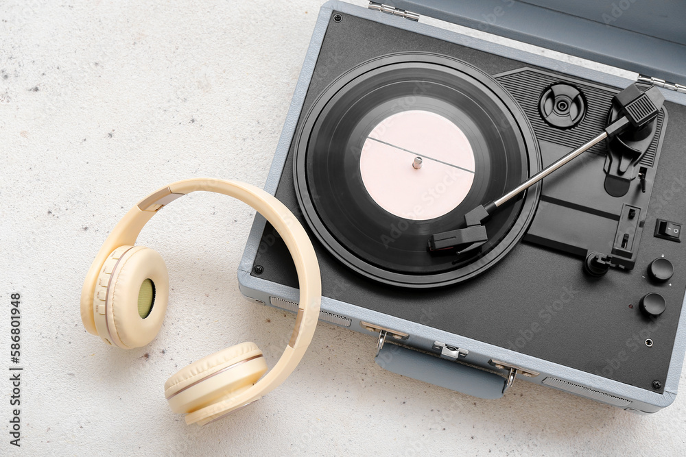 Record player with vinyl disk and headphones on light background