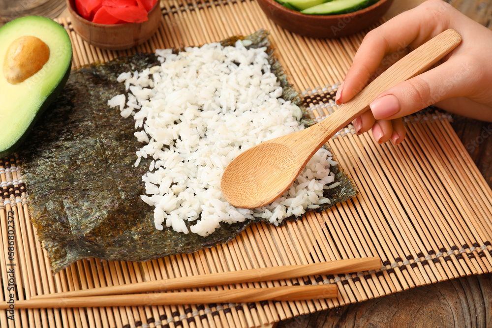 Woman preparing sushi rolls on bamboo mat, closeup