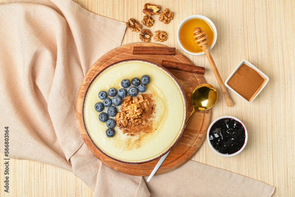 Bowl of tasty semolina porridge with blueberry, honey, cinnamon, jam and nuts on light wooden backgr