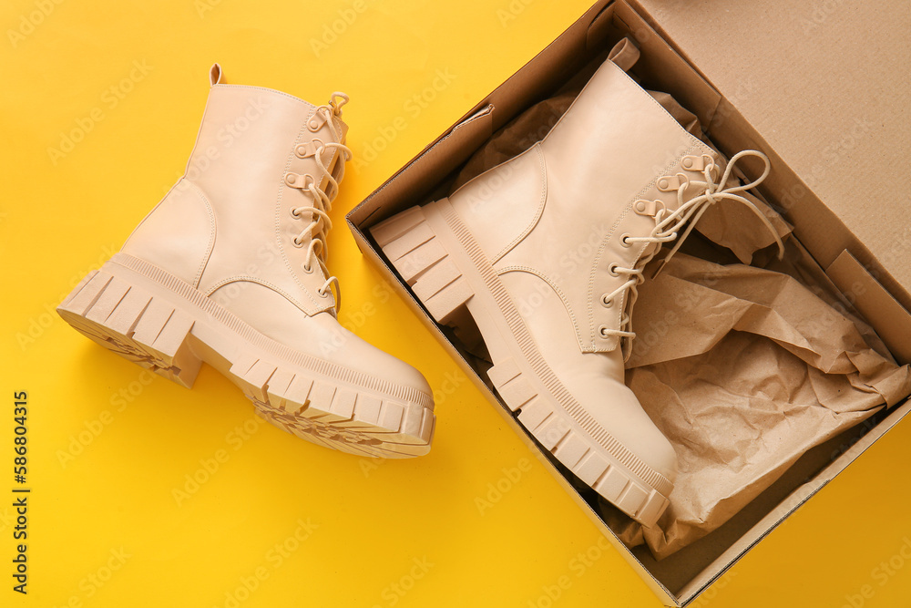 Cardboard box with stylish shoes on yellow background