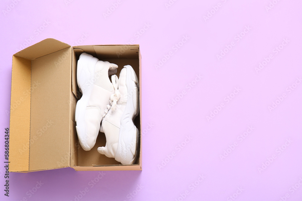 Cardboard box with sports shoes on lilac background