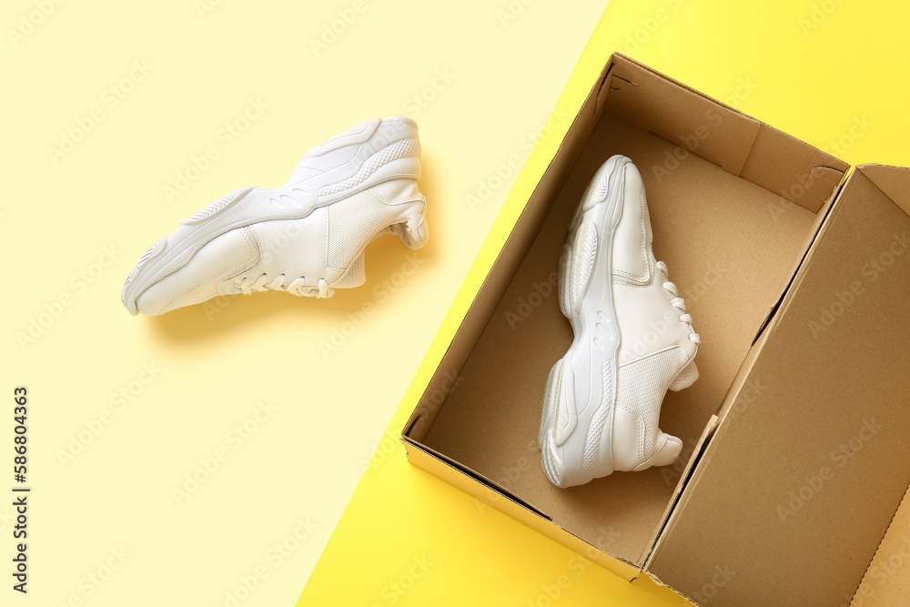 Cardboard box with sports shoes on color background