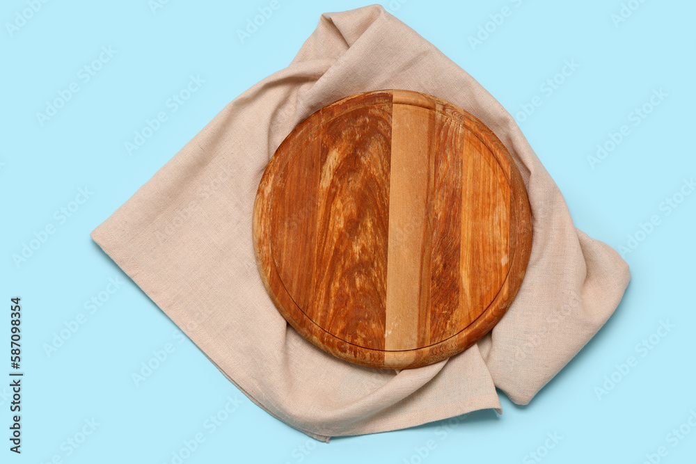 Wooden cutting board with napkin on color background