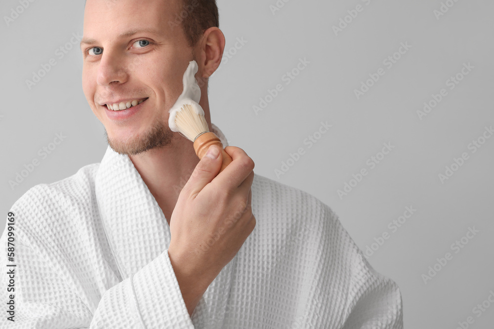 Young man applying shaving foam on face against light background