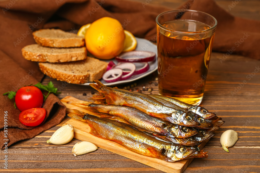 Board with delicious smoked capelin, glass of beer and plate with snacks on wooden background