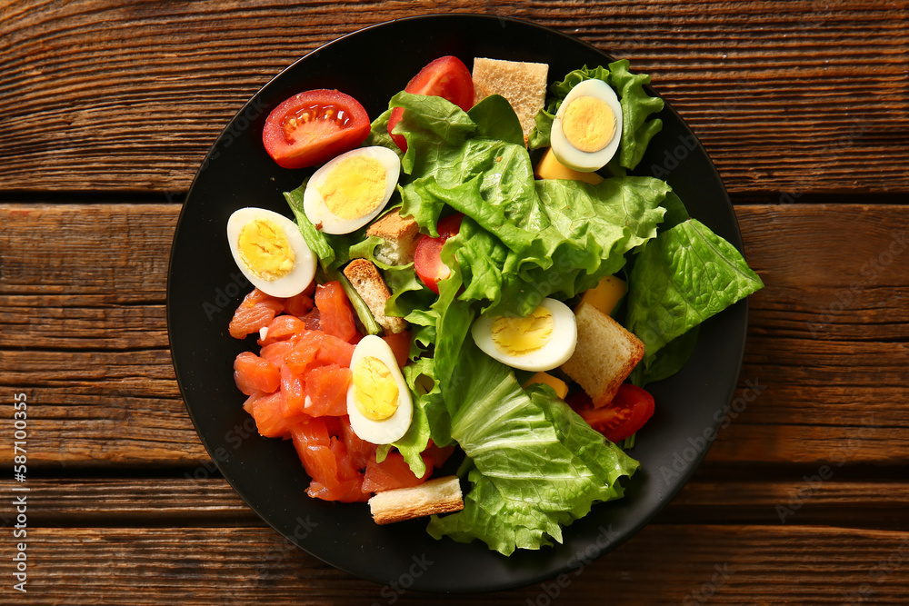 Plate of delicious salad with boiled eggs and salmon on brown wooden background