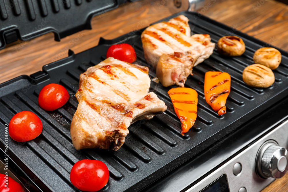 Modern electric grill with tasty steaks and vegetables on wooden background