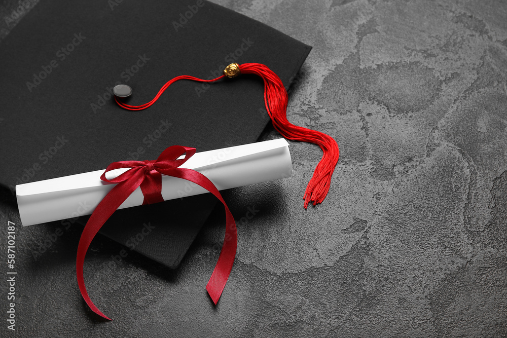 Diploma with red ribbon and graduation hat on black table