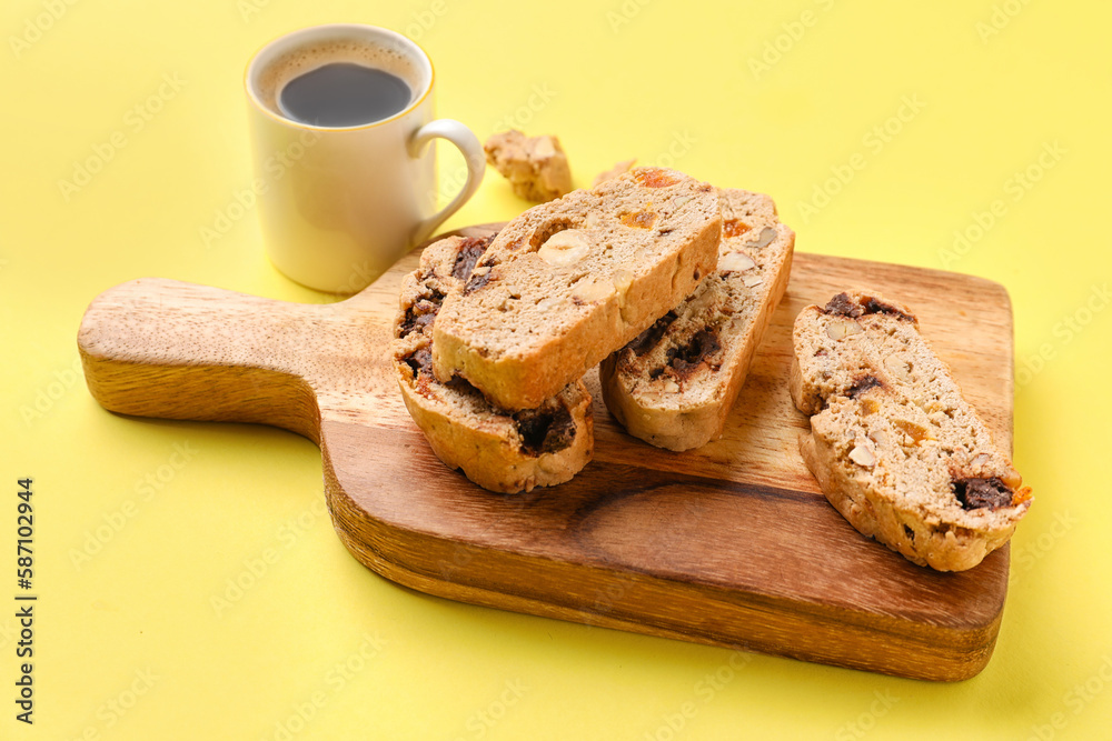 Board with delicious biscotti cookies and cup of coffee on yellow background