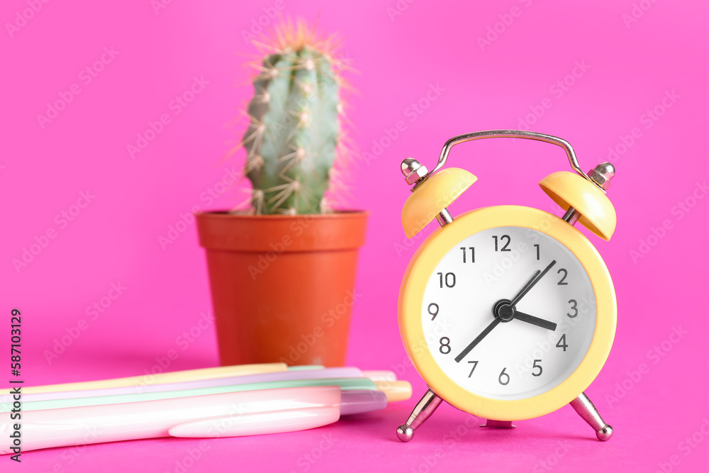 Alarm clock, pens and cactus on pink background