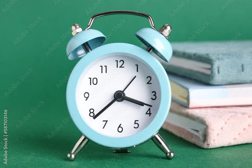 Alarm clock and notebooks on green background, closeup