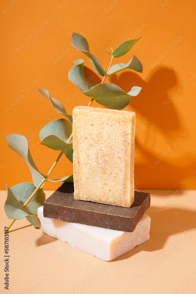 Stack of natural soap bars and eucalyptus branch on color background