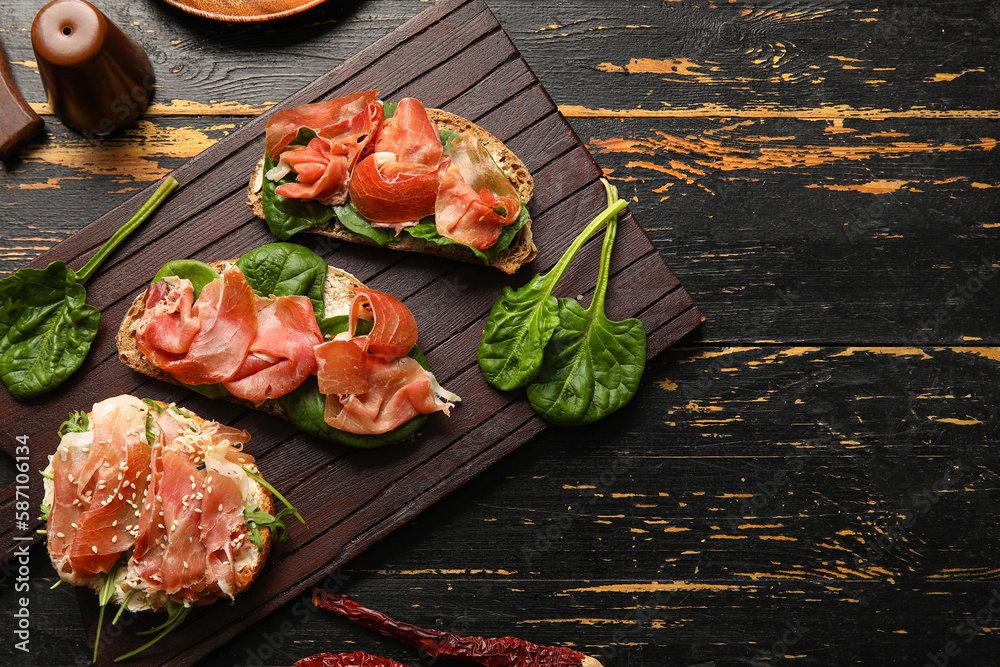 Board of tasty bruschettas with ham on dark wooden background