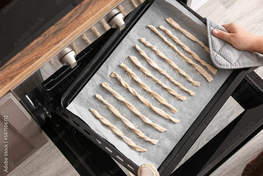 Woman putting baking sheet with Italian Grissini into oven, closeup