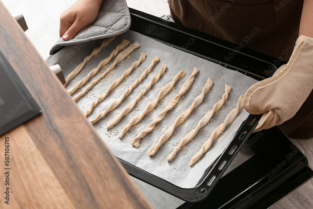 Woman putting baking sheet with Italian Grissini into oven, closeup