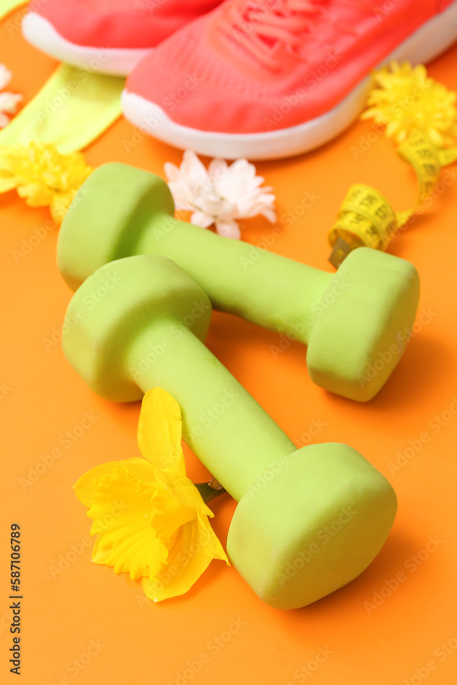 Dumbbells with spring flowers on color background, closeup