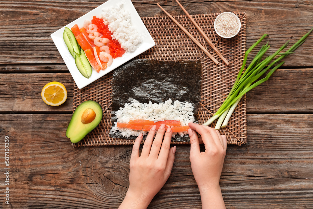 Woman preparing sushi rolls on wooden background