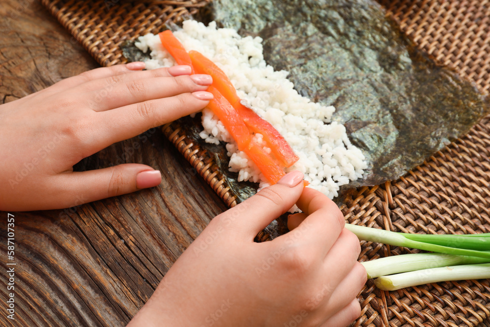 Woman preparing sushi rolls on wooden background, closeup