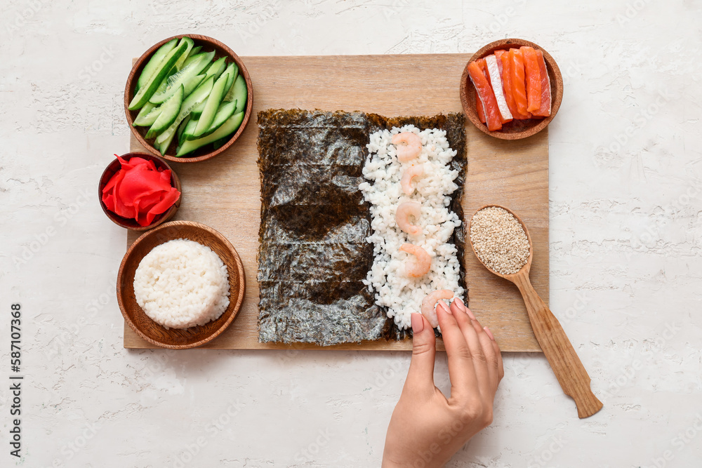 Woman preparing sushi rolls on light background