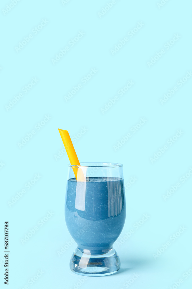 Glass of tasty blue smoothie with straw on color background