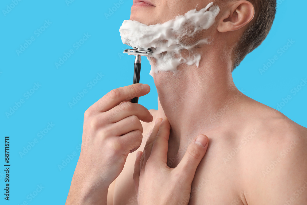 Young man shaving against light blue background, closeup