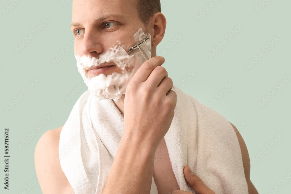 Young man shaving against green background